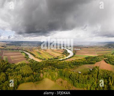 Vista aerea del meandro del fiume San che si snoda attraverso campi agricoli e foreste autunnali sotto un cielo nuvoloso drammatico a Dynow, Voivodato della Precarpazia Foto Stock