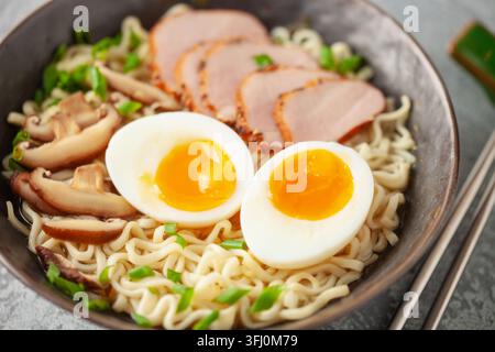 Spaghetti di ramen giapponesi con fetta di maiale, funghi shiitake e uova in una ciotola nera Foto Stock