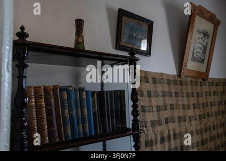 Vecchio scaffale pieno di libri rilegati in pelle antichi e opere d'arte incorniciate sul muro nella stanza Foto Stock