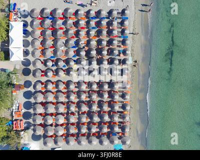 Veduta aerea di file di ombrelloni di paglia e lettini sulla spiaggia sabbiosa di Katarinies Paralia, Grecia. Foto Stock