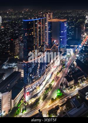 Vista aerea di grattacieli moderni illuminati e tracce di luce del traffico sulle strade di notte a Surabaya, Giava Orientale, Indonesia. Foto Stock