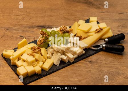 piatta di formaggi assortiti con uva e noci su un vassoio da portata, preparata come antipasto gourmet per intrattenere e abbinare con il vino Foto Stock