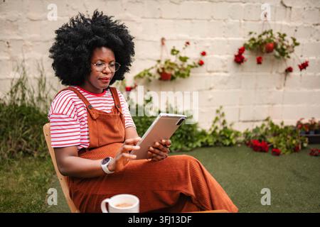 Donna nera che si rilassa nel cortile usando un tablet digitale Foto Stock