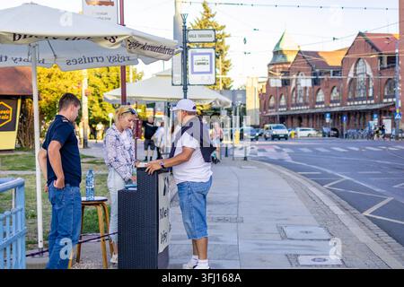 8 agosto 2026, Wroclaw, Polonia. Un venditore di biglietti che parla con turisti a un banco informazioni per la prenotazione di escursioni all'aperto vicino alla storica Hala Targowa Foto Stock