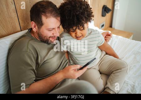 Padre e figlio che si legano sul letto usando uno smartphone Foto Stock