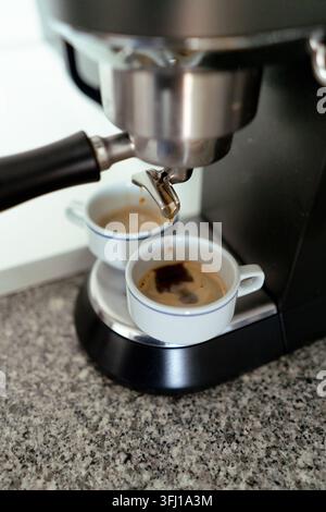 Macchina per l'espresso che gocciola caffè fresco in due tazze bianche su un bancone di granito Foto Stock