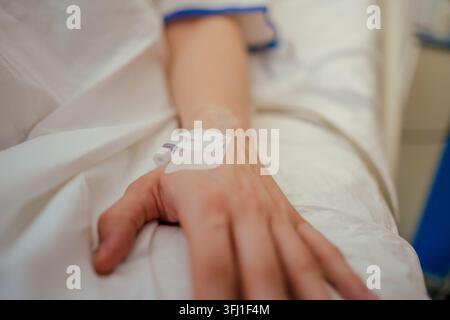 Mano di paziente con un catetere IV su un lenzuolo bianco da ospedale durante il trattamento Foto Stock