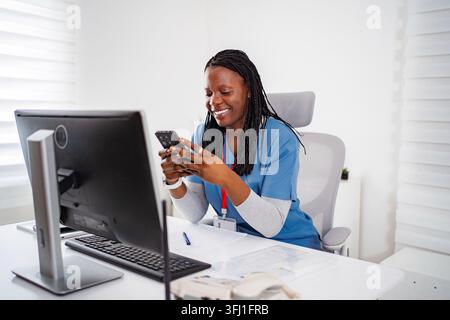 Infermiera sorridente che usa uno smartphone in una clinica d'ufficio Foto Stock