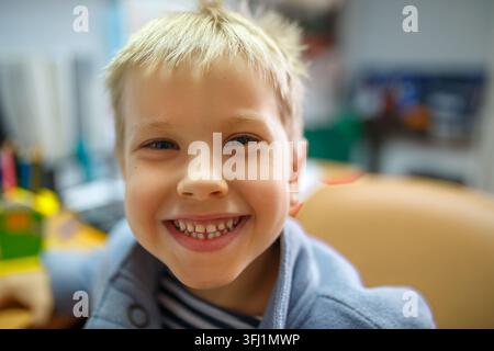 Ragazzo biondo che ride con una felpa blu alla scrivania della scuola, primo piano Foto Stock