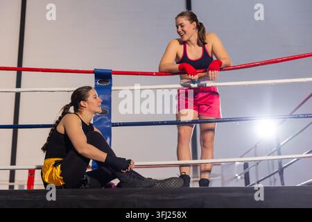 Due pugili che si appoggiano sulle corde, seduti in un anello da boxe indossando pantaloncini rosa e avvolgimenti a mano. Sparring, atleti, palestra, allenamento, partner, candido, le Foto Stock