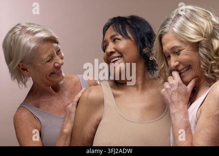 Diverse amiche che posano vicine in uno studio beige caldo con canottiere neutre e piccoli orecchini Foto Stock