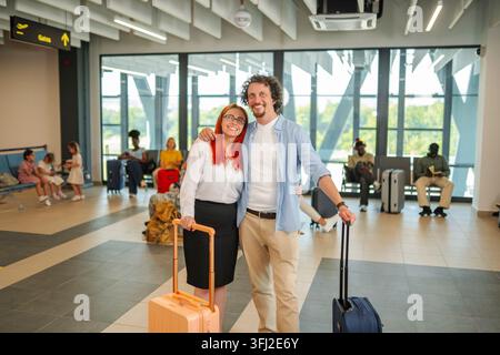 Una giovane coppia sorridente in piedi nell'area d'attesa dell'aeroporto con le valigie, pronta per la partenza Foto Stock