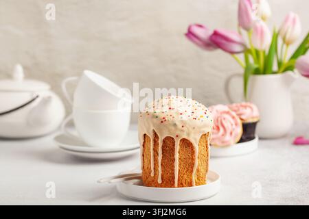 Torte di Pasqua Kulich, tulipani e utensili bianchi per una cerimonia del tè su uno sfondo luminoso. Concetto di vacanza Foto Stock