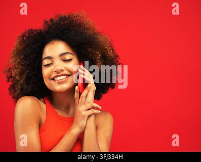 Ritratto di studio di una donna birazziale con smartphone rosso e capelli a texture afro Foto Stock