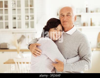 Coppia matura felice che si abbraccia nella cucina della loro casa. Foto Stock