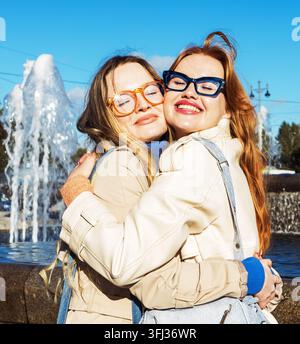 Due giovani donne che godono di un momento gioioso all'aperto vicino a una fontana in una città primaverile in una giornata di sole. Foto Stock