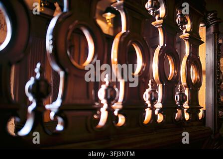 Una ringhiera in legno dettagliata presenta ritagli circolari e disegni intricati, illuminata da una luce soffusa, che evidenzia l'artigianalità in un interno elegante Foto Stock