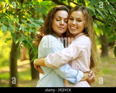 Madre matura e figlia adulta che si abbracciano nel parco in una giornata estiva Foto Stock