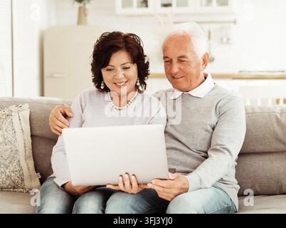 Coppia di anziani che usa un computer portatile seduti sul divano a casa Foto Stock