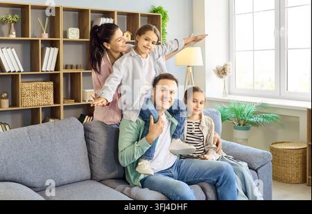 Genitori felici con due bambini che si abbracciano e giocano sul divano in un accogliente interno domestico Foto Stock