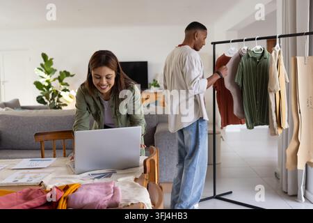 Coppia afroamericana che lavora in soggiorno organizzando tessuti, laptop, espositore di abiti, spazio per la copia Foto Stock