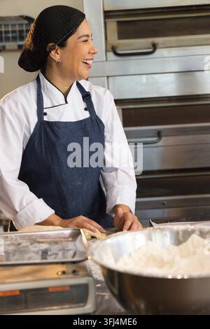 Chef donna con giacca bianca e grembiule che impasta il pane in una cucina professionale con ciotola per impastare. Farina, pasticceria, acciaio inossidabile, ripido Foto Stock