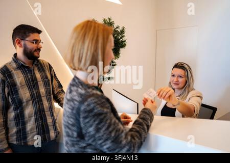 Addetto alla reception che consegna la chiave magnetica a una cliente che fa il check-in Foto Stock