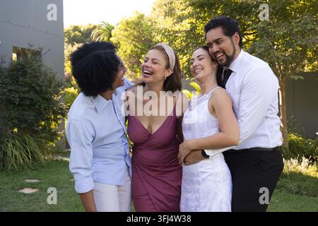 Amici diversi che ridono e si abbracciano sul prato del cortile, indossando un vestito di pizzo bianco e una cravatta nera. All'aperto, giardino, gruppo, celebrazione, insieme, jo Foto Stock