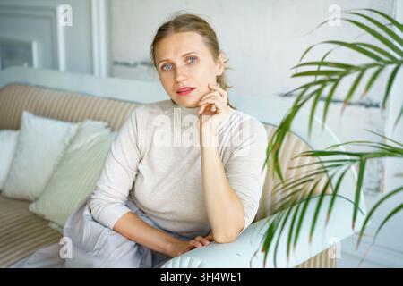 Donna in un maglione a collo alto beige lavorato a maglia in una casa luminosa Foto Stock