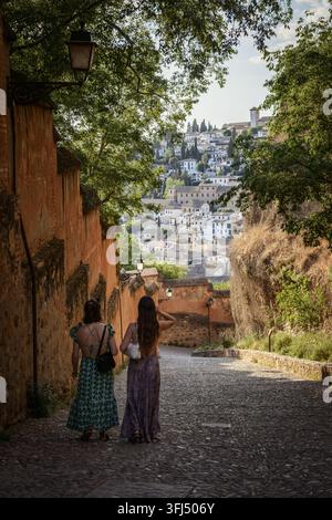Due donne camminano lungo la strada acciottolata Cuesta del Rey Chico a Granada, Andalusia, Spagna, durante un pomeriggio soleggiato di primavera. Foto Stock
