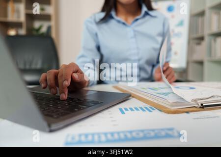 Donna d'affari che lavora su un laptop con documenti di contabilità finanziaria in un ufficio moderno Foto Stock