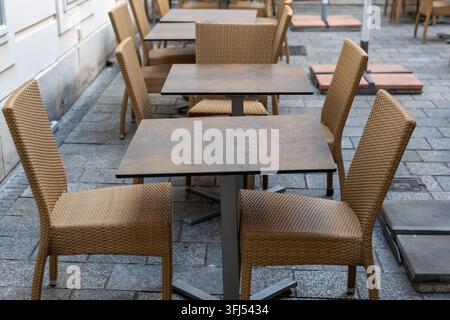Area di seduta vuota del caffè all'aperto con sedie intrecciate e tavoli quadrati su una terrazza lastricata. Foto Stock