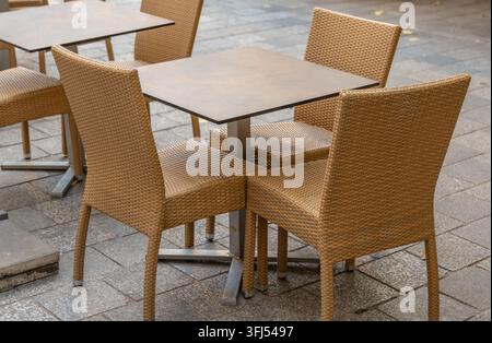 Sedere di vimini vuoti circondano tavoli quadrati su una terrazza esterna lastricata. Foto Stock