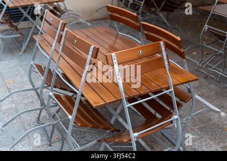 Tavoli e sedie da caffè in legno impilati si trovano su una tranquilla terrazza all'aperto. Foto Stock
