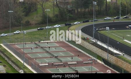 Area sportiva di una scuola superiore americana con campo da tennis, campo da calcio e persone che giocano sul campo da pickleball. Vista aerea. Auto sulla strada. Giorno soleggiato a Foto Stock