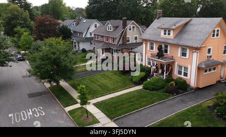 Casa color pesca con portico con balcone si trova accanto alle case vicine su una strada alberata a South Orange, New Jersey, con marciapiedi e prati curati Foto Stock