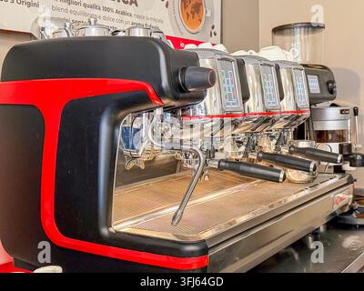Milazzo - ME - IT - Set 09, 2026: Macchina da caffè commerciale con corpo rosso e nero, gruppi di erogazione cromati, portafiltri e tubo del vapore in un bar Foto Stock