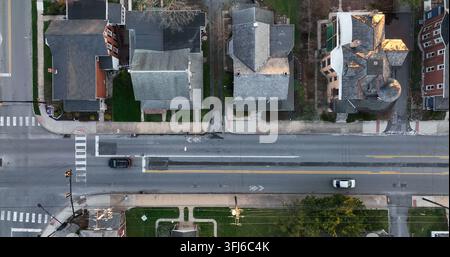Vista aerea dall'alto di una strada urbana. Le foglie verdi degli alberi riflettono la luce dell'ora dorata. Un'auto nera attraversa la città, Elizabethtown, Pennsylvania. Foto Stock