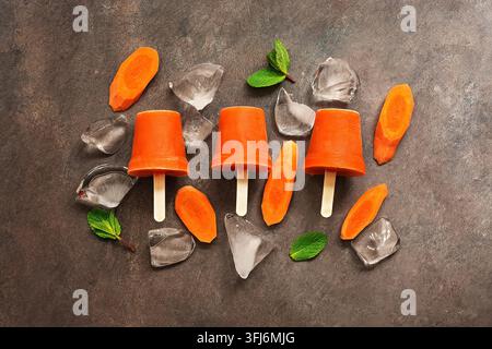 Sano dessert vegano estivo. Gelati. Succo di carota congelato su bastone, sfondo marrone scuro. Vista dall'alto, disposizione piatta, spazio di copia Foto Stock