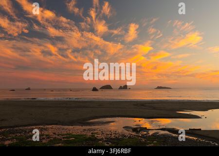 Tramonto, nuvole cumulus che sovrastano la costa nord del Pacifico, bassa marea, torrente interno che sfocia nella baia, isole rocciose, California. Foto Stock
