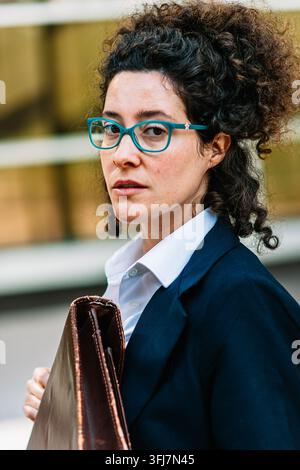 Donna d'affari professionista con capelli ricci che indossa occhiali e porta una valigetta Foto Stock