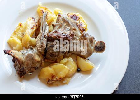 Vista dall'alto di spalla d'agnello arrosto con patate dorate al forno, un piatto tradizionale di carne cotto al forno italiano su un piatto bianco Foto Stock