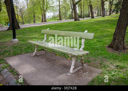 Vecchia panchina di legno nel giardino pubblico verde con erba e alberi Foto Stock