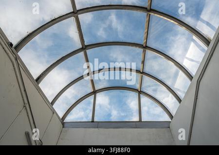Vista ad angolo basso di un lucernario in vetro curvo con cielo azzurro e nuvole bianche Foto Stock