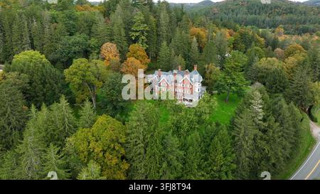 Ripresa aerea rotazionale di un drone di una villa in mattoni tra una foresta di pini e foglie autunnali mutevoli. Grande casa in una zona remota, panoramica e tranquilla, Woodstock, Vermont Foto Stock