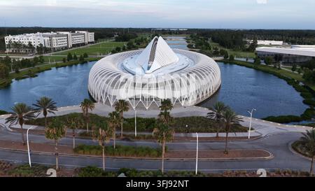 Il campus della Florida Polytechnic University risplende all'alba, il distinto edificio circolare dell'innovazione si erge da un lago riflettente circondato da palme Foto Stock