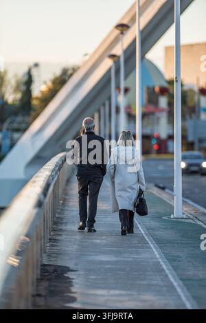 Una coppia matura attraversa il ponte Barqueta a Siviglia, Andalusia, Spagna durante un bellissimo tramonto invernale. L'uomo parla al telefono. Foto Stock