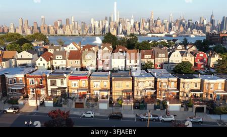 Case a schiera colorate fiancheggiano la strada accanto alle auto parcheggiate a Union City, nel New Jersey, il One World Trade Center e l’Empire State Building si ergono dall’altra parte del fiume Hudson Foto Stock