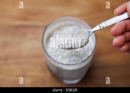 Pudding di chia servito in un bicchiere con un cucchiaio tenuto sopra Foto Stock