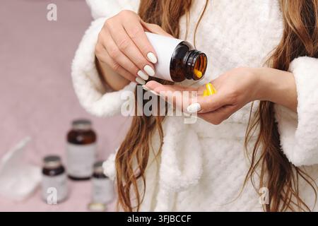 Donna che versa capsule gialle di integratori da una bottiglia marrone nella propria mano. Sfondo sanitario per vitamine, nutrizione, integrazione benessere. Foto Stock